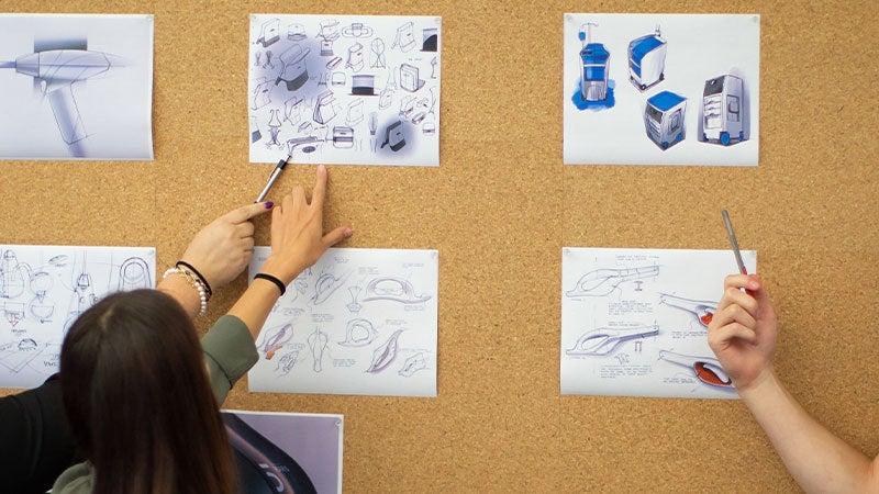 People reviewing schematics pinned on a cork board