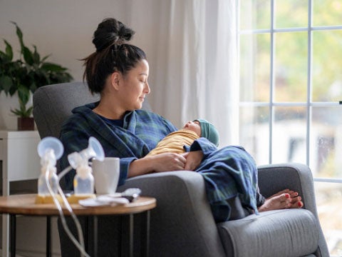 Mother holding her baby while sitting next to a breast pump