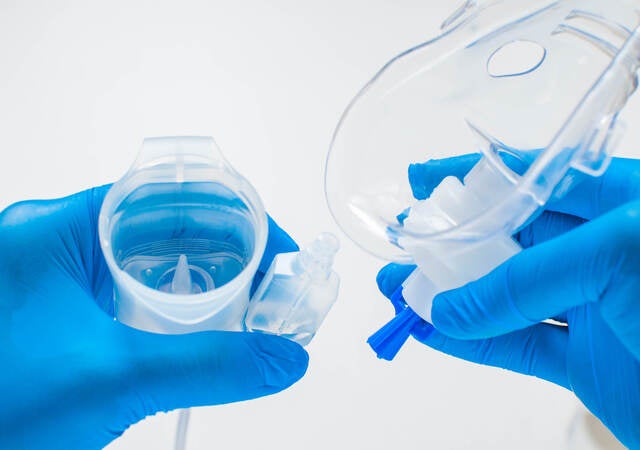 A young healthcare worker with blue gloves is preparing an asthma nebulizer on a white background