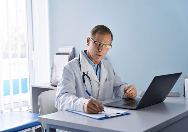 Doctor sitting at a desk taking notes from a labtop