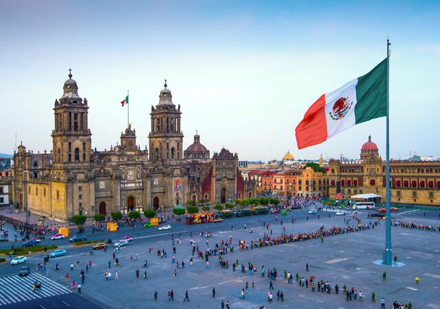The Mexican flag flies over the Zocalo, the main square in Mexico City. The Metropolitan Cathedral faces the square, also referred to as Constitution Square.