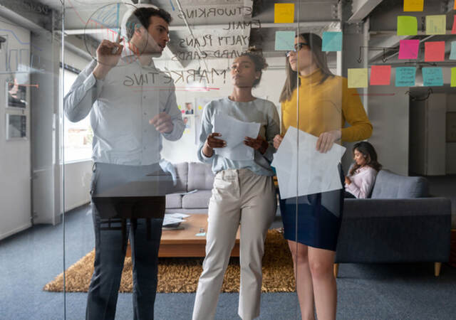 Three coworkers collaborating together in front of a glass wall