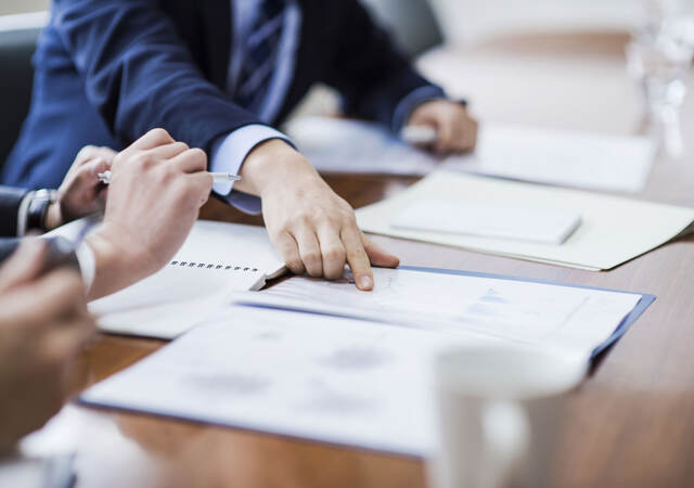 Person in a suit pointing to reports laying on a conference table during a meeting