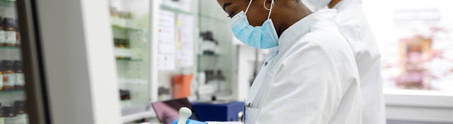 Two scientists making medicine at a laboratory. Doctors working together at pharmacy lab wearing protective work wear.