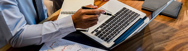 Person sitting at a desk taking notes and looking at a laptop