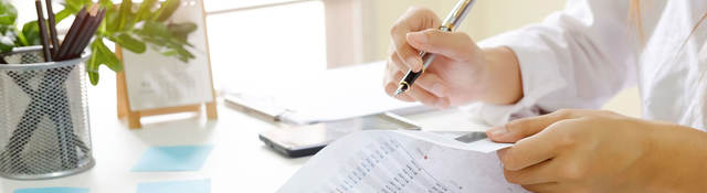 Person sitting at desk reviewing documents with a pen