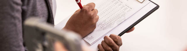 Person taking notes on a clipboard while someone tests a medical device