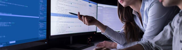 Two people in a dark office reviewing data on a computer