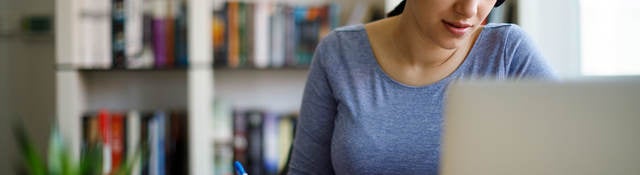 Woman with headphones taking notes and looking at a laptop