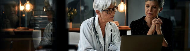 Two medical professionals reviewing notes on a laptop