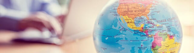 Close of a little globe with a person using a laptop in the background