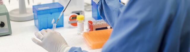 Scientist using a pipet while holding a vial