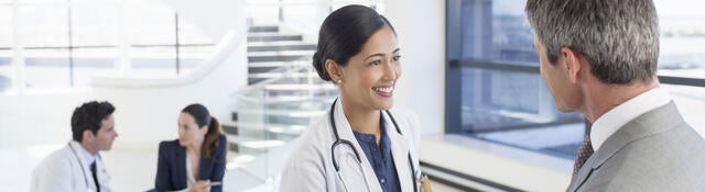 A doctor shaking hands with a business professional while another doctor has a meeting in the background