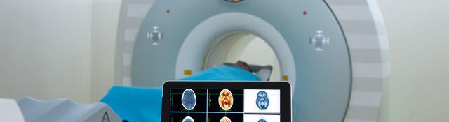 Doctor viewing an MRI on a tablet while standing in front of the patient laying inside the MRI