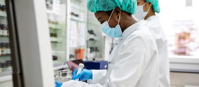 Two scientists making medicine at a laboratory. Doctors working together at pharmacy lab wearing protective work wear.