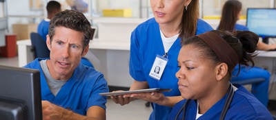 Three nurses surround a computer