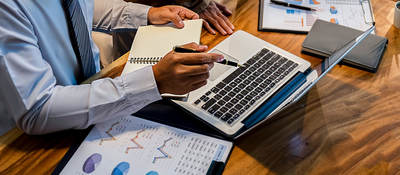 Person sitting at a desk taking notes and looking at a laptop