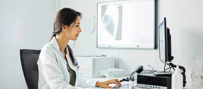 Confident doctor using computer at desk. A medical professional is working in clinic. They are wearing lab coat.