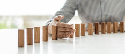 Dominos standing on a table with a hand in between two of the dominos