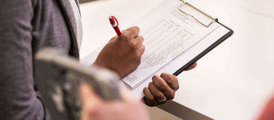 Person taking notes on a clipboard while someone tests a medical device