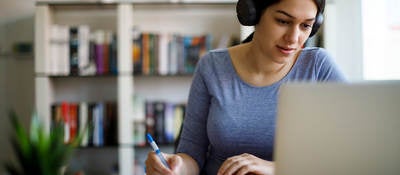 Woman with headphones taking notes and looking at a laptop