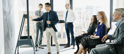 Group of colleagues having a meeting while one presents on a board