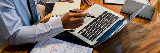 Person sitting at a desk taking notes and looking at a laptop