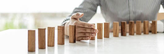 Dominos standing on a table with a hand in between two of the dominos