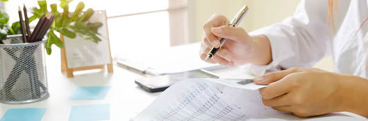 Person sitting at desk reviewing documents with a pen