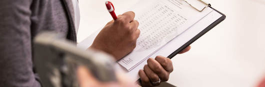 Person taking notes on a clipboard while someone tests a medical device