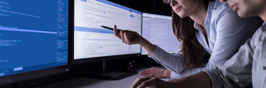 Two people in a dark office reviewing data on a computer