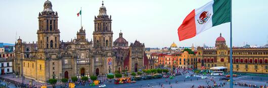 The Mexican flag flies over the Zocalo, the main square in Mexico City. The Metropolitan Cathedral faces the square, also referred to as Constitution Square.
