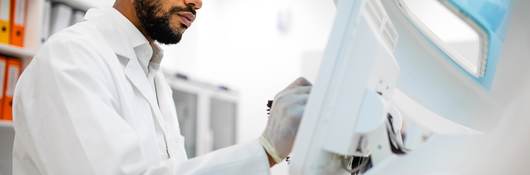 Scientist in lab coat working at the computer screen.