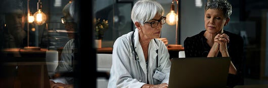 Two medical professionals reviewing notes on a laptop
