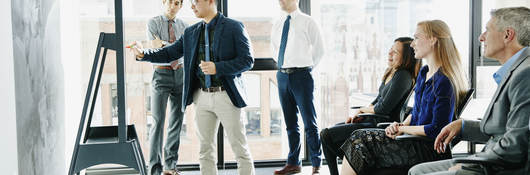 Group of colleagues having a meeting while one presents on a board