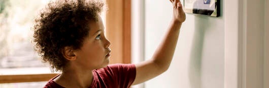 Boy checking smart thermostat.