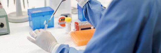 Scientist using a pipet while holding a vial