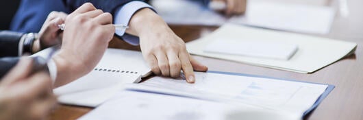 Person in a suit pointing to reports laying on a conference table during a meeting