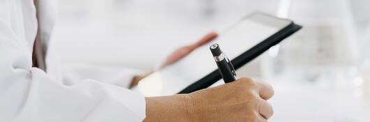 Closeup of a medical professional reading a tablet and making notes on paper while standing in a lab