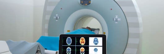 Doctor viewing an MRI on a tablet while standing in front of the patient laying inside the MRI