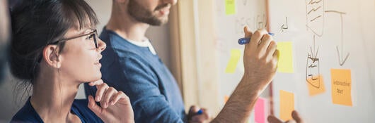 Two colleagues are creating a process map on a whiteboard.