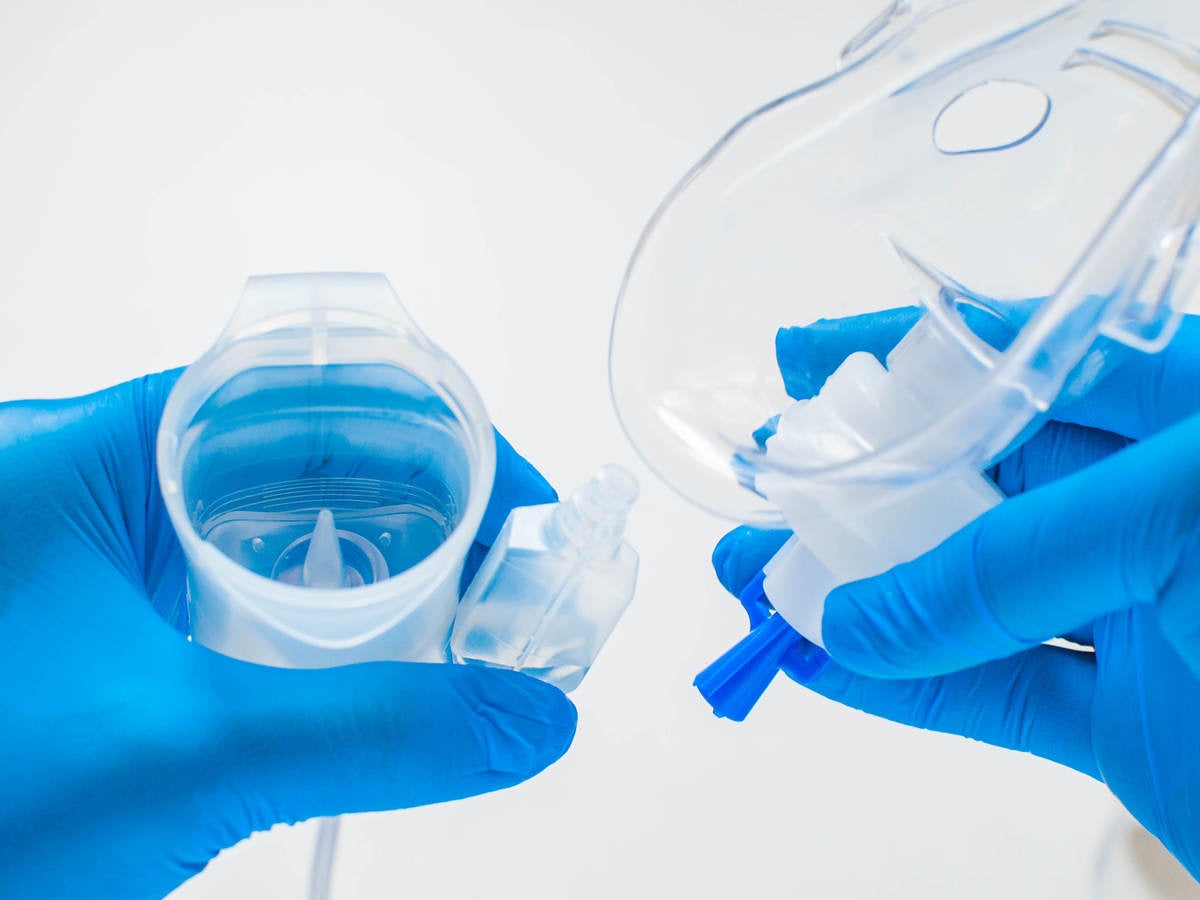 A young healthcare worker with blue gloves is preparing an asthma nebulizer on a white background