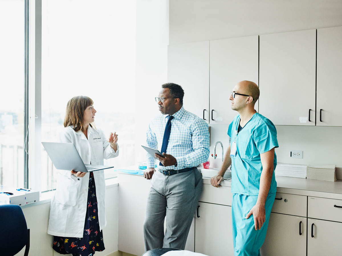 Doctors gather and discuss while holding laptop and papers