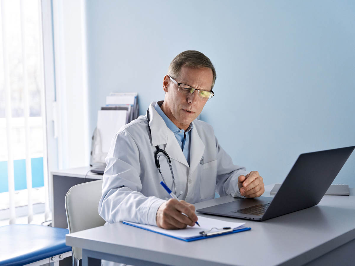 A doctor working on a laptop and taking notes