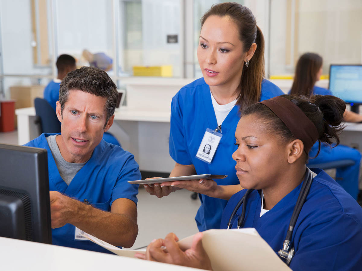 Three nurses surround a computer