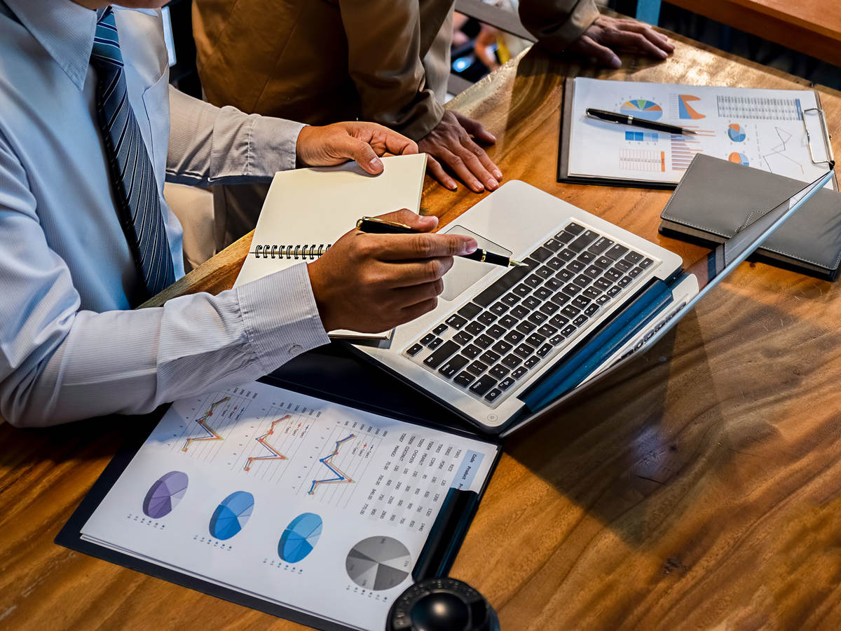 Person sitting at a desk taking notes and looking at a laptop