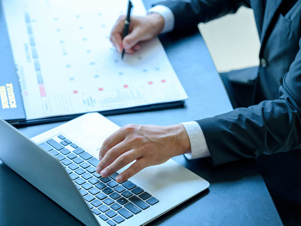 A person in a suit is taking notes and working on a laptop