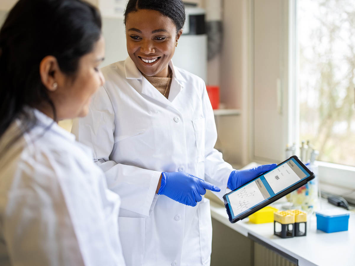 Lab technician smiling and pointing to a tablet