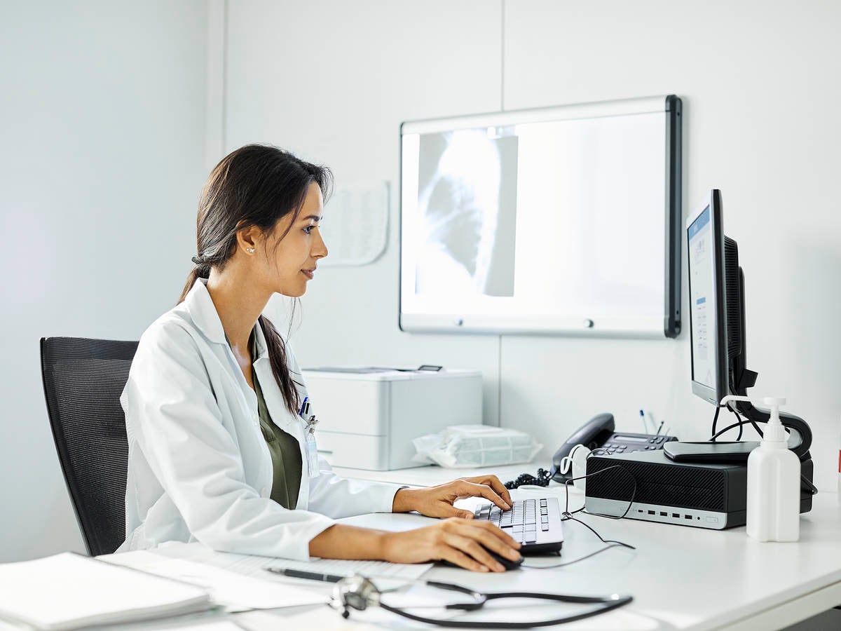 Confident doctor using computer at desk. A medical professional is working in clinic. They are wearing lab coat.