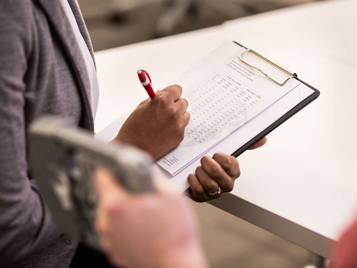 Person taking notes on a clipboard while someone tests a medical device